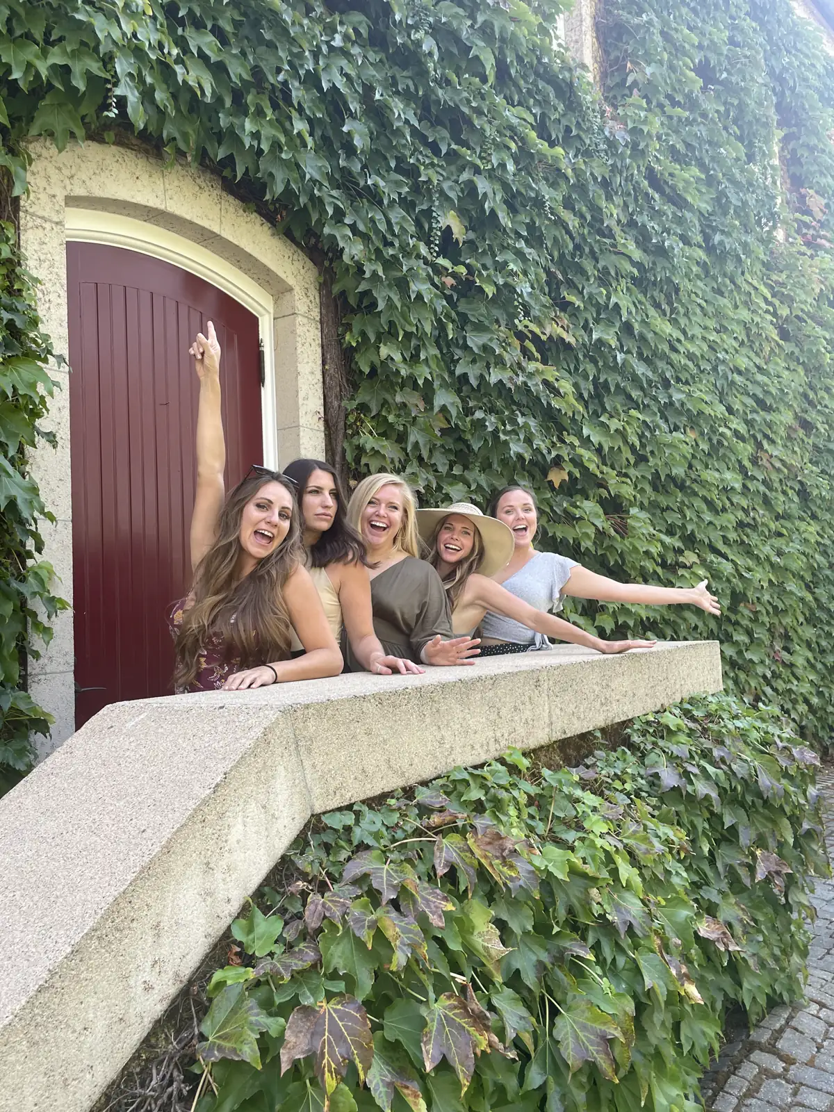A group of women sitting on an ivy-covered wall by an arched door