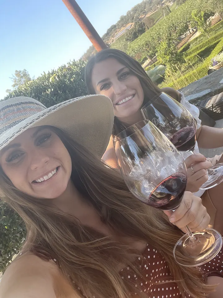 Two women in sun hats taking a selfie with glasses of wine