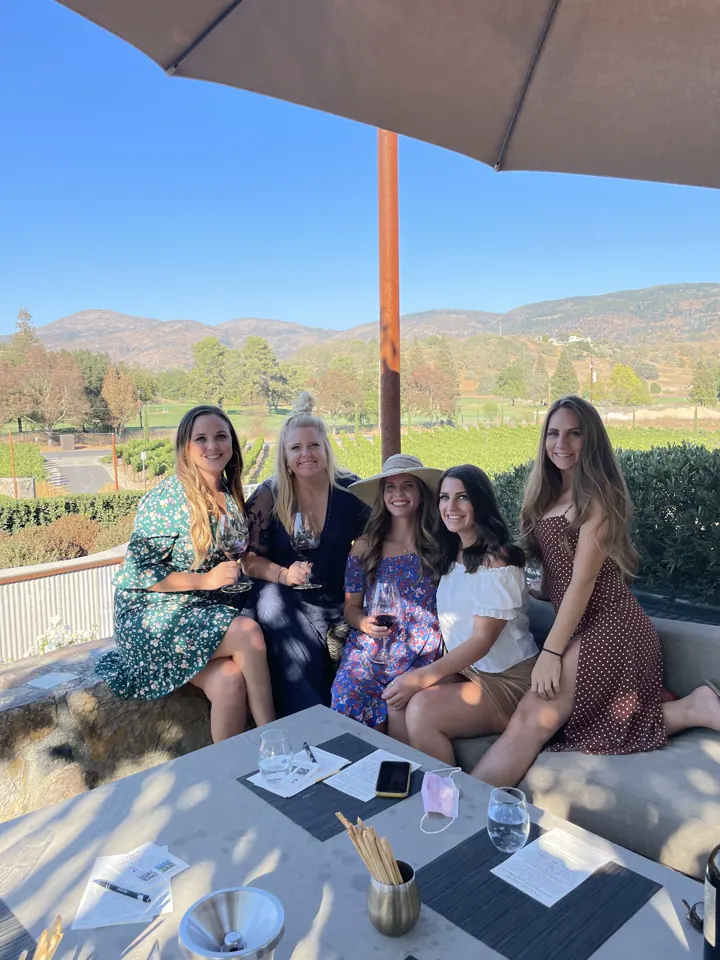 A group of women at a winery terrace table with vineyards and mountains behind
