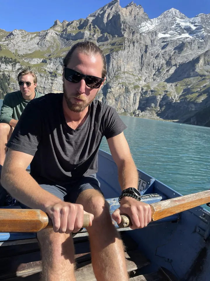 Colin rowing a wooden boat on the lake with cliffs behind