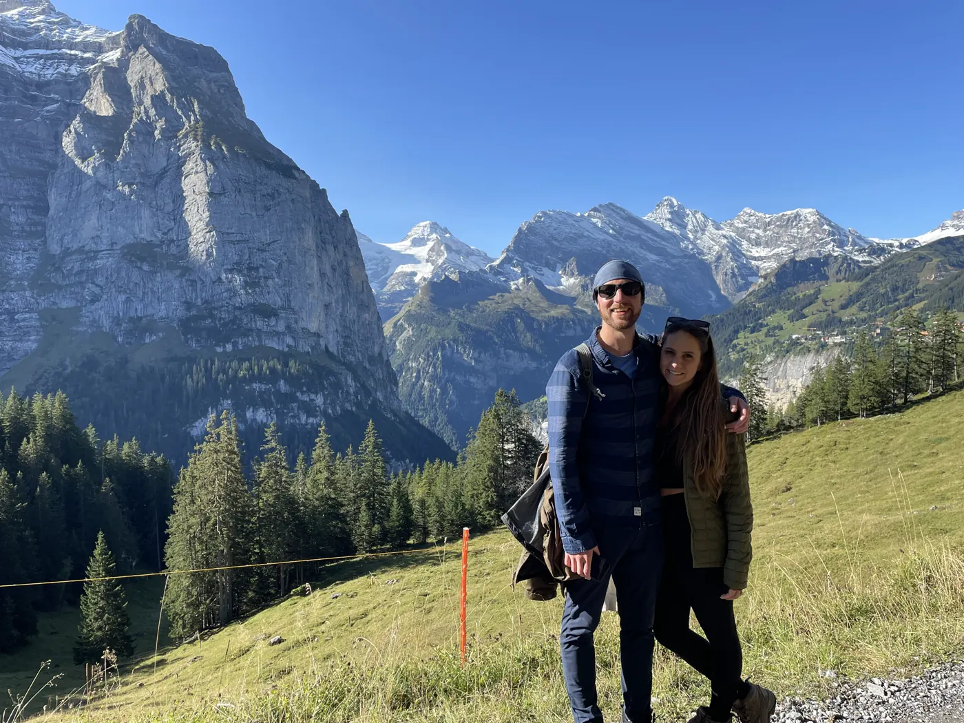 Colin and Angela standing on a grassy slope with snowy peaks behind