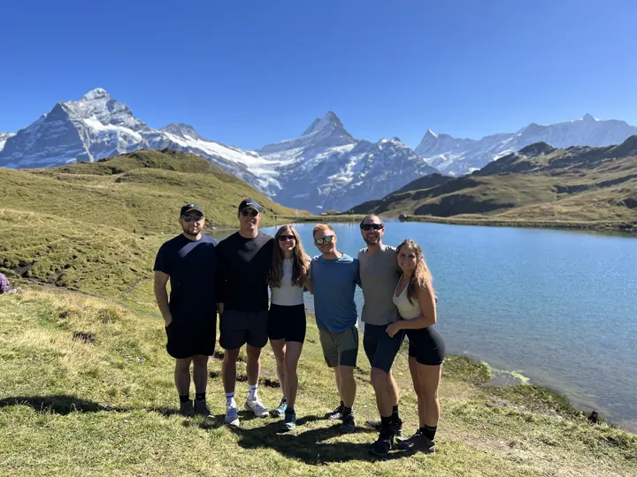 Group of friends standing by an alpine lake with mountains behind
