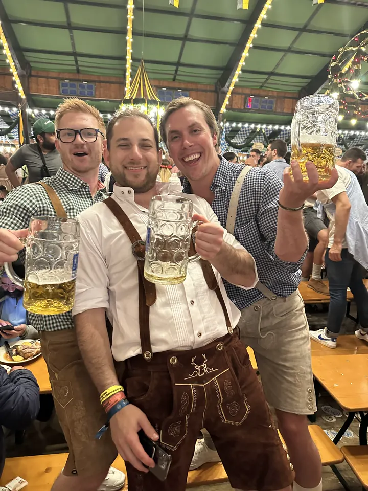 Friends in lederhosen raising big beer steins in a beer tent