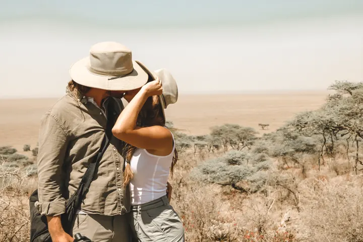 A person in a safari hat looking through binoculars over the plains