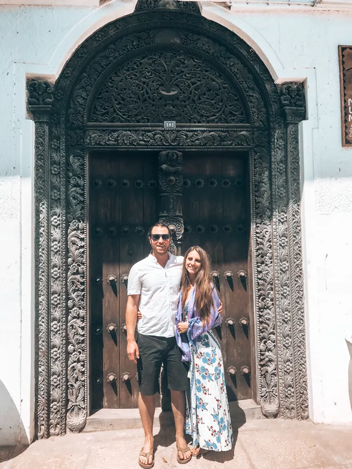 A couple standing in front of an ornate carved wooden arched door