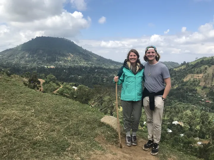 A couple standing on a green hillside with a volcanic peak behind them