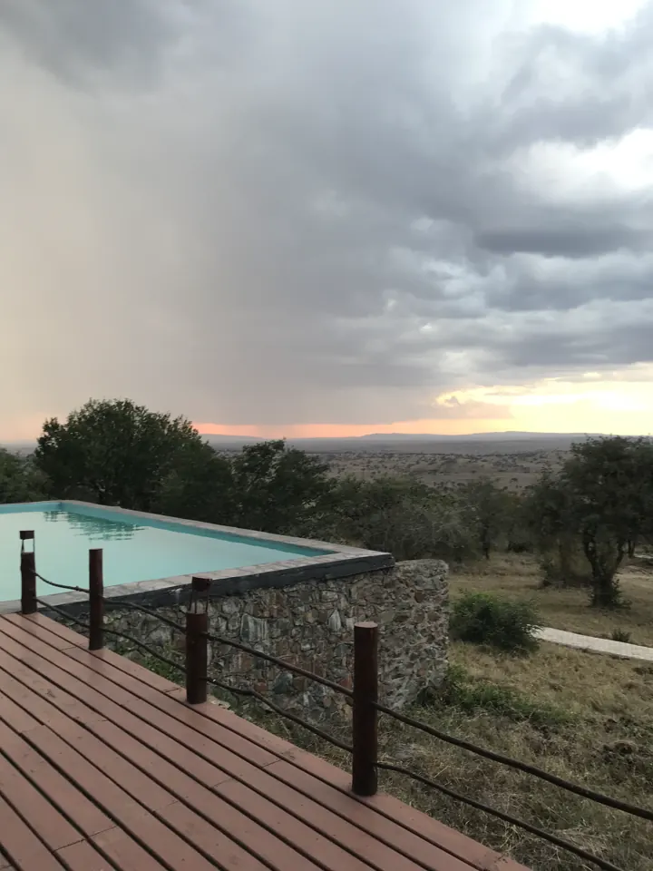 An infinity pool on a wooden deck overlooking plains with a distant rainstorm