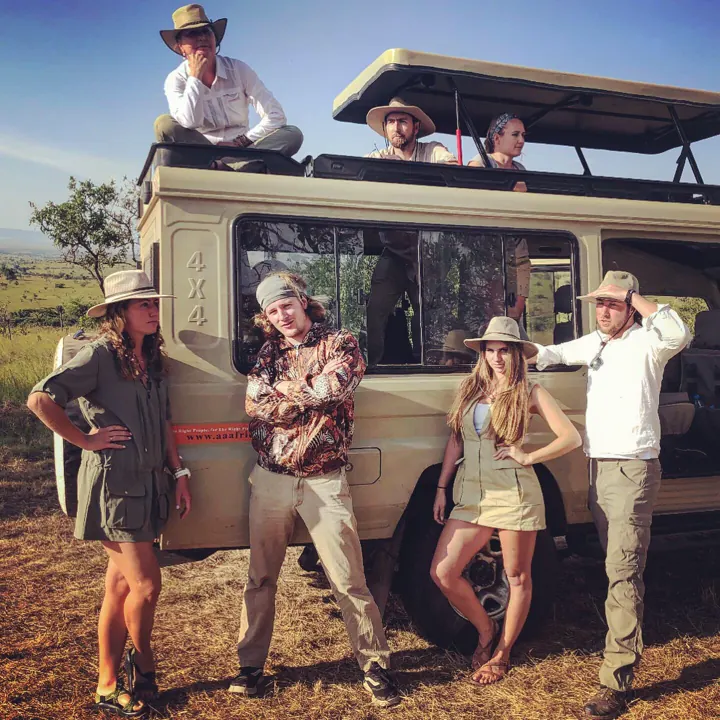 A group of family members in safari hats posing on and beside a safari vehicle