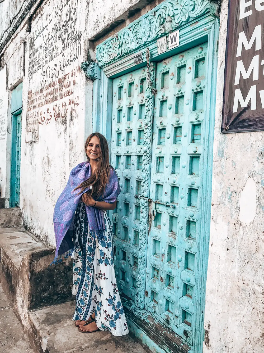 A woman in a flowing blue dress beside a weathered turquoise carved door