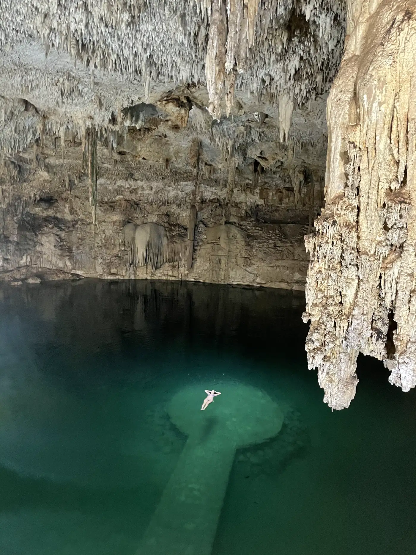 A cave cenote with stalactites and a round stone platform in emerald water