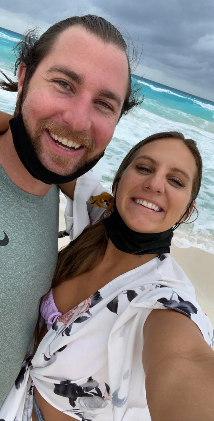 A couple taking a selfie by the sea, one pulling down a face mask