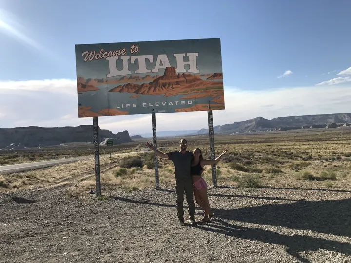 A couple standing by a 'Welcome to Utah' sign in the desert